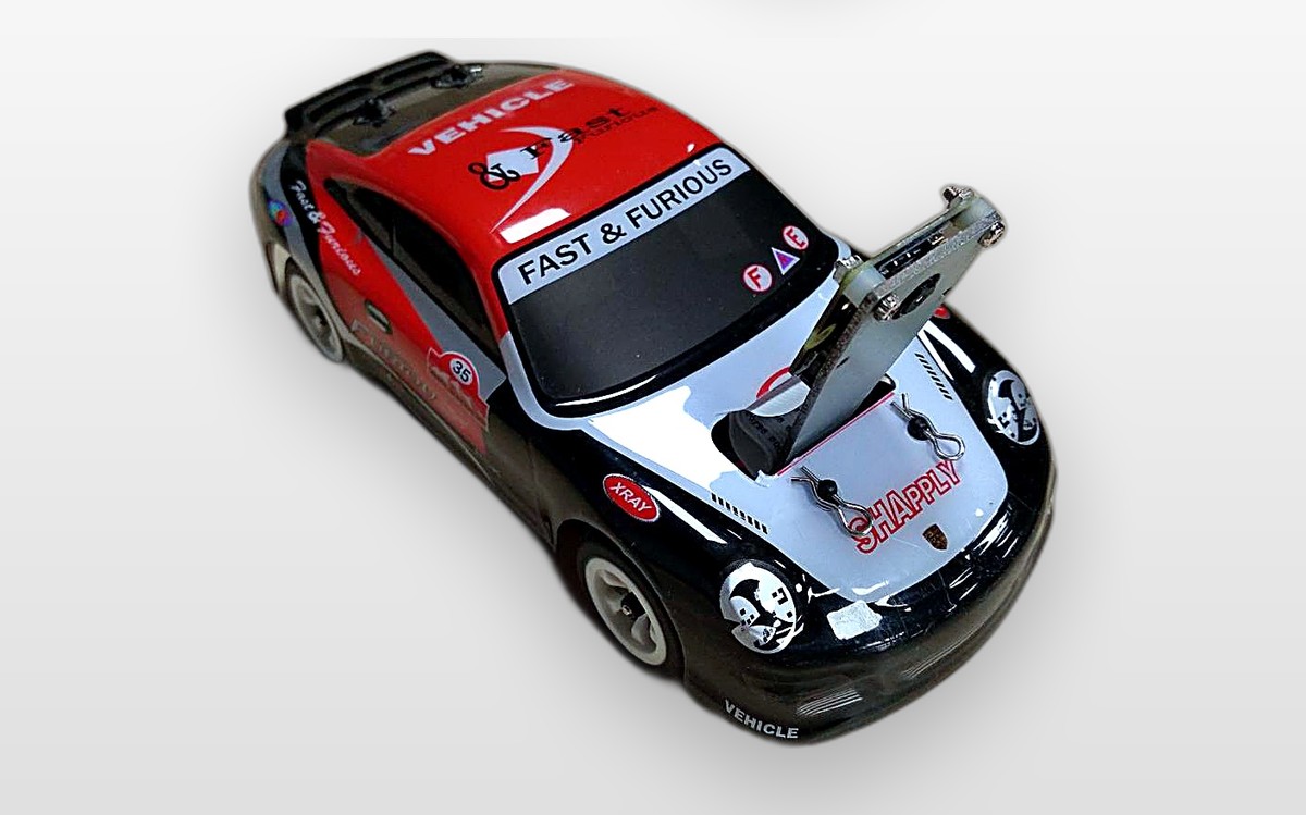 TopRacer Car 實車照：黑紅塗裝的 1/28 賽車，車頭裝著相機支架，攝影棚淺灰背景。